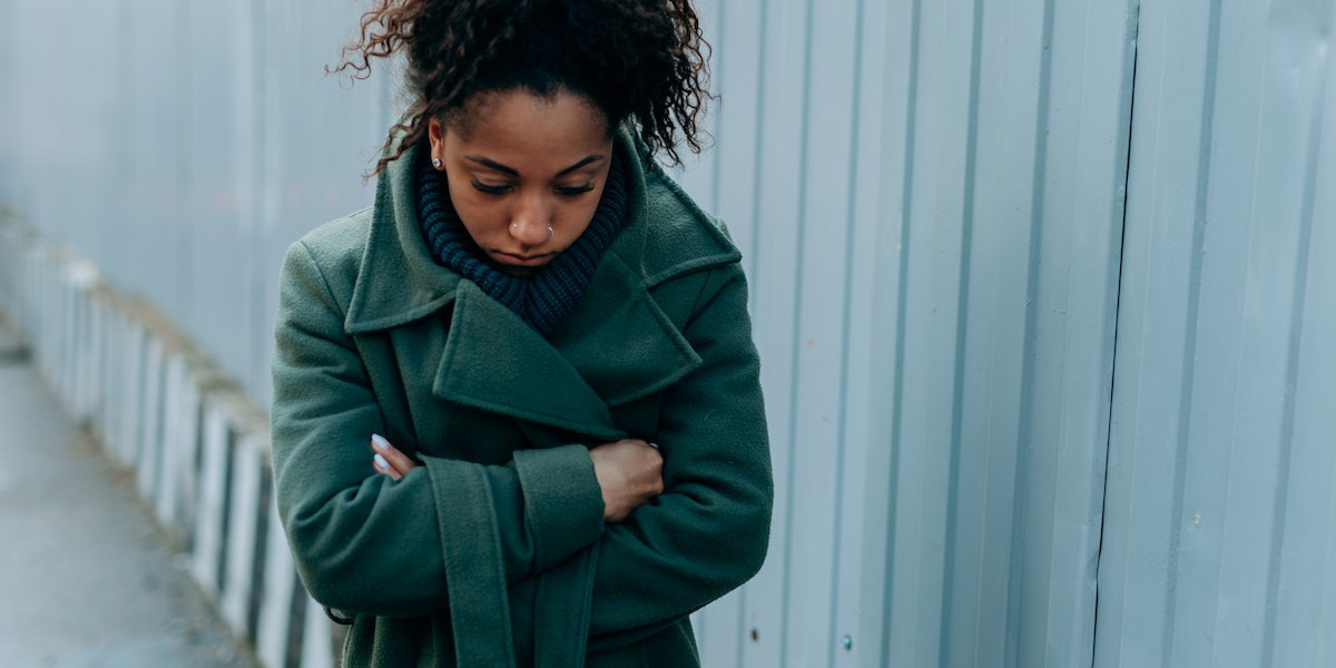 A Sad Woman in Green Coat Leaning on Brown Brick Wall