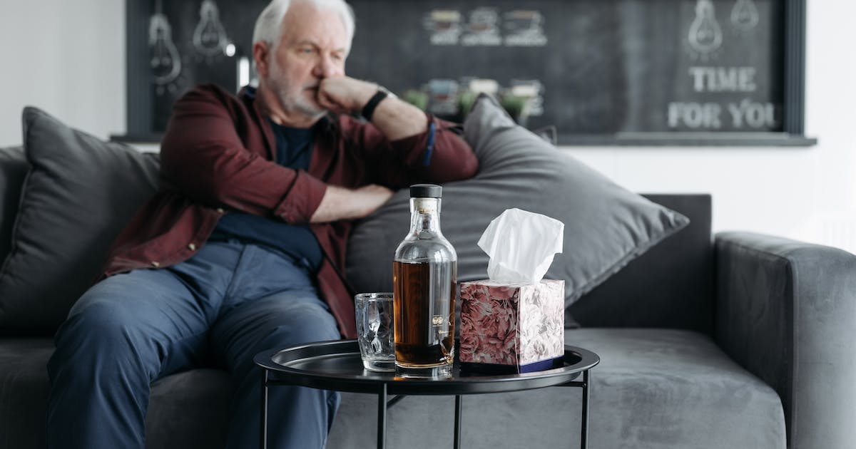 older man sitting on the couch looking at at bottle of whiskey