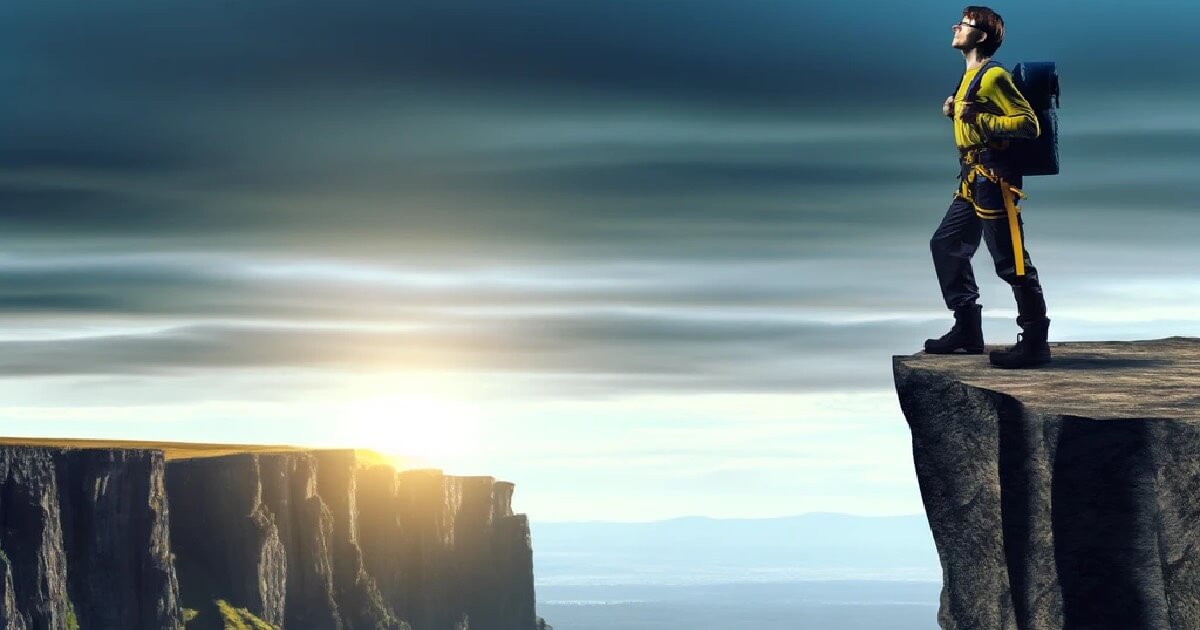 A man with a backpack stands on the edge of a cliff, overlooking a breathtaking view.